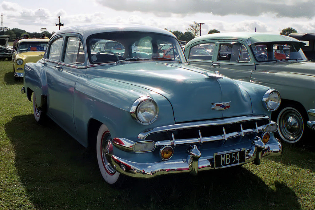 Blue 1954 Chevrolet four-door sedan viewed from the front and side at a car show.